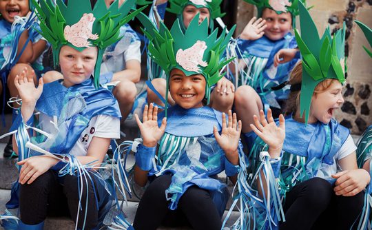 School children dressed in colour blue costumes looking happy.