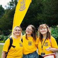 Three volunteers in yellow Hat Fair t-shirts smiling and looking happy.