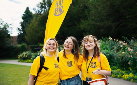 Three volunteers in yellow Hat Fair t-shirts smiling and looking happy.