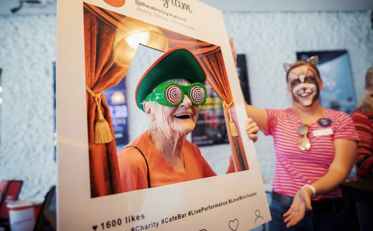 A person holding up a theatre branded frame and wearing googly eyes looking happy.