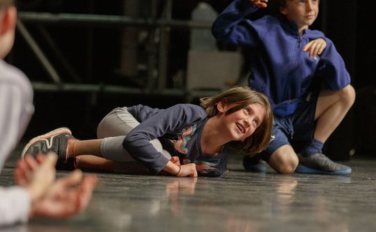 A young person on lying on stage during a theatre workshop.