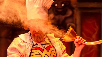 A person dressed as a chef and holding a funnel with flour puffing out of it.