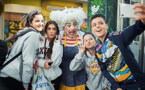 A panto dame taking a selfie with four young people.