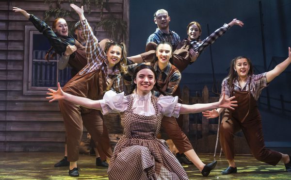 A group of panto performers posing on stage with their arms out.
