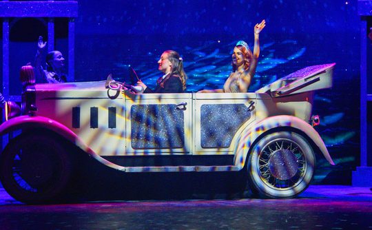 Cinderella in a car waving, on stage.