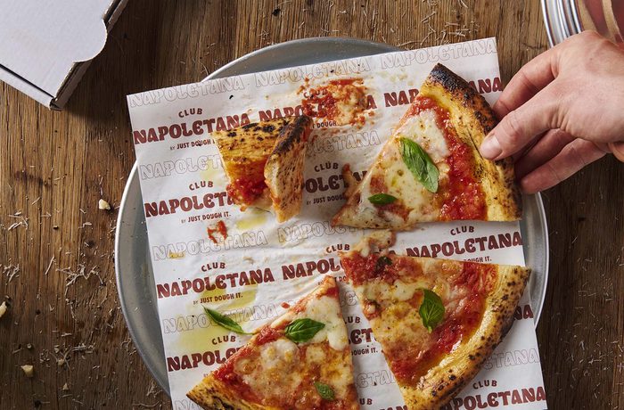 A hand reaching for a slice of pizza.