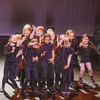 A group of young people dressed in dark clothing performing movement work.