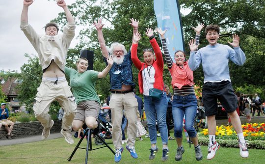 Performers and judges of Top Hat 2025 all jumping in joy outside on grass.