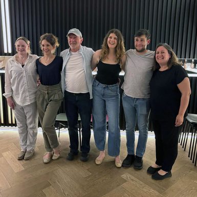 A group of six people standing in a row with their arms around each other.