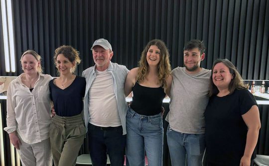 A group of six people standing in a row with their arms around each other.