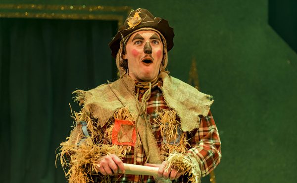 A panto performer as Scarecrow from The Wizard of Oz holding a scroll.