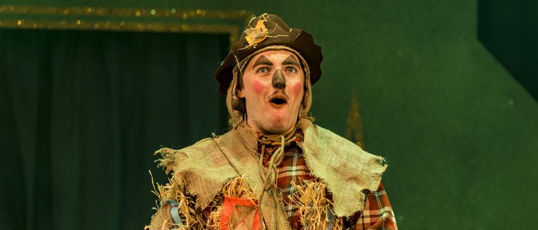 A panto performer as Scarecrow from The Wizard of Oz holding a scroll.