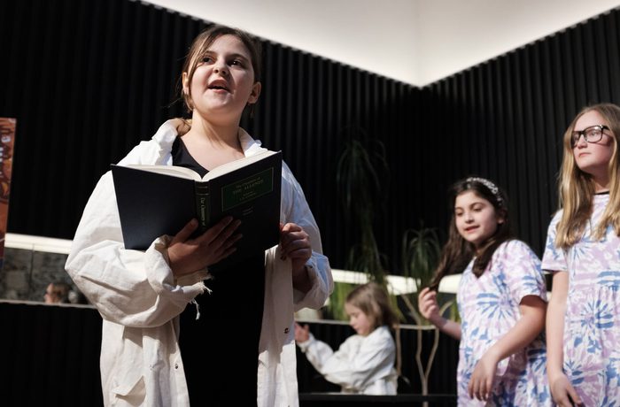A young person holding a book and reading out to the audience.