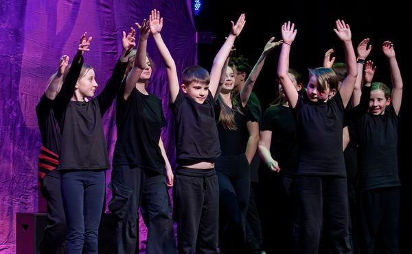 Young performers dressed in black clothing with their hands in the air.