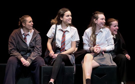 Young performers in school uniform on stage and looking happy.