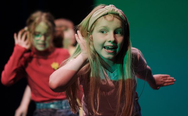 Young person looking happy with a hand up to their ear trying to listen.