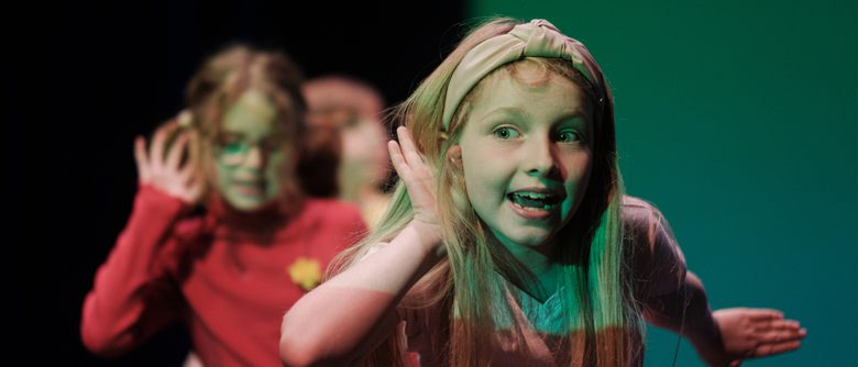 Young person looking happy with a hand up to their ear trying to listen.