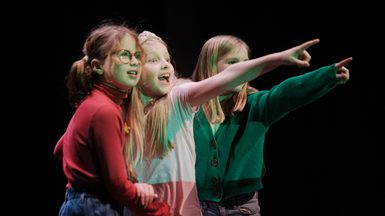 Three young performers looking happy and pointing.