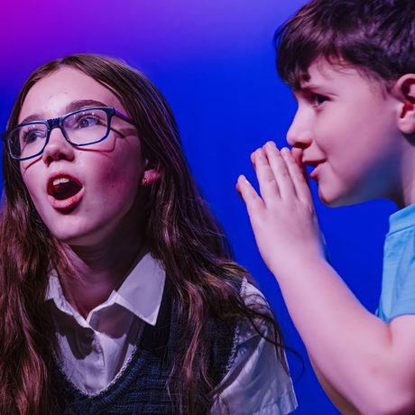 Two young performers whispering on stage.