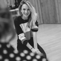 A black and white photo of a person with long hair sat on their knees and smiling.
