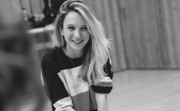 A black and white photo of a person with long hair sat on their knees and smiling.