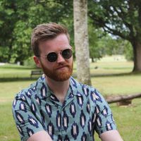 A person sat in a woodland park with a vibrant shirt, beard and sunglasses.