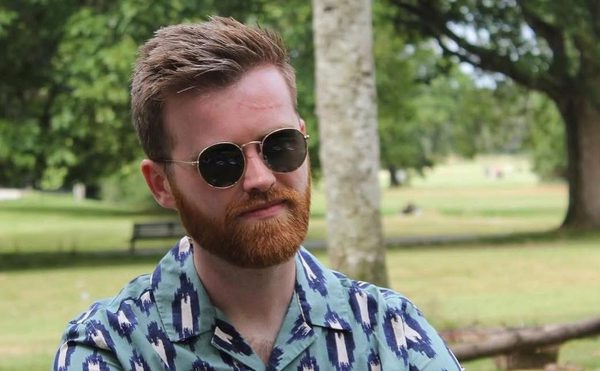 A person sat in a woodland park with a vibrant shirt, beard and sunglasses.