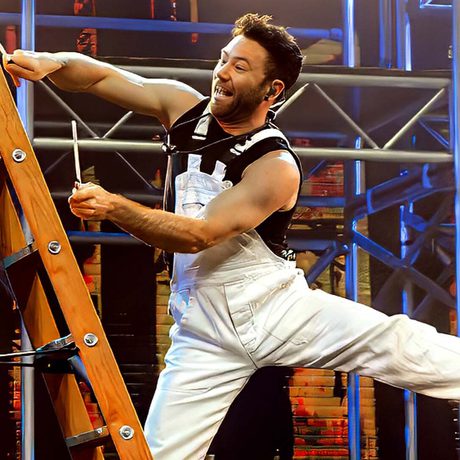 A performer dressed as a painter and decorator on a ladder