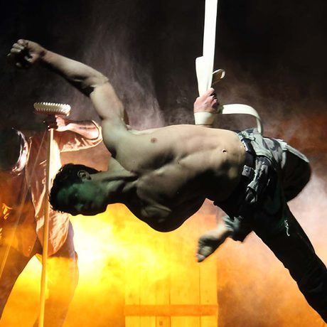 A shirtless performer suspended from a rope