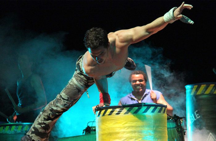 A shirless performer doing acrobatics on a tin barrel